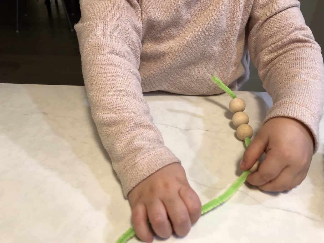 Toddler threading beads onto pipe cleaner