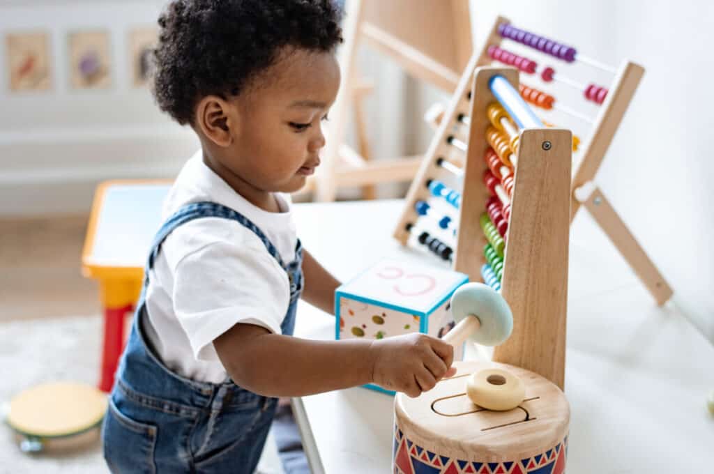 Montessori Toys - Baby playing with wooden toys on a white shelf
