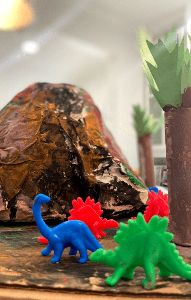 plastic dinosaurs in front of a paper mache volcano