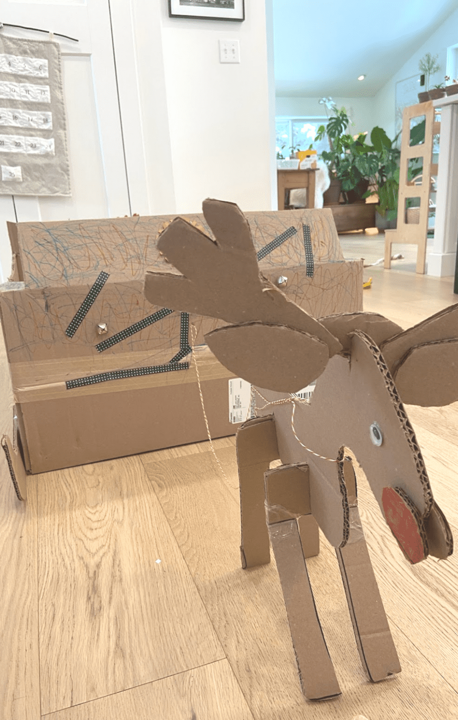 A cardboard reindeer with a googly eye and a red nose and a cardboard sleigh.