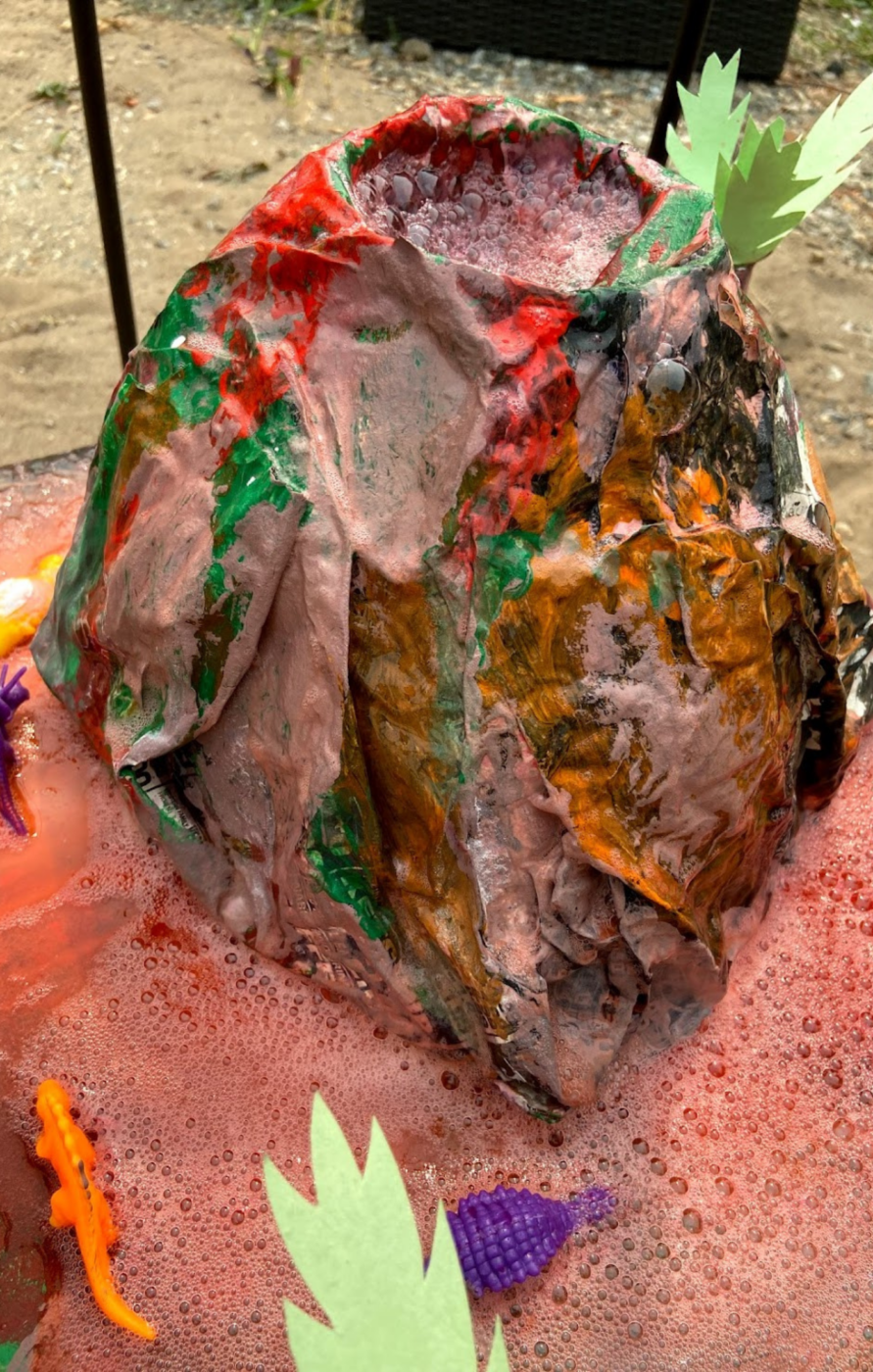 Paper mache volcano with little plastic dinosaurs and red "lava".