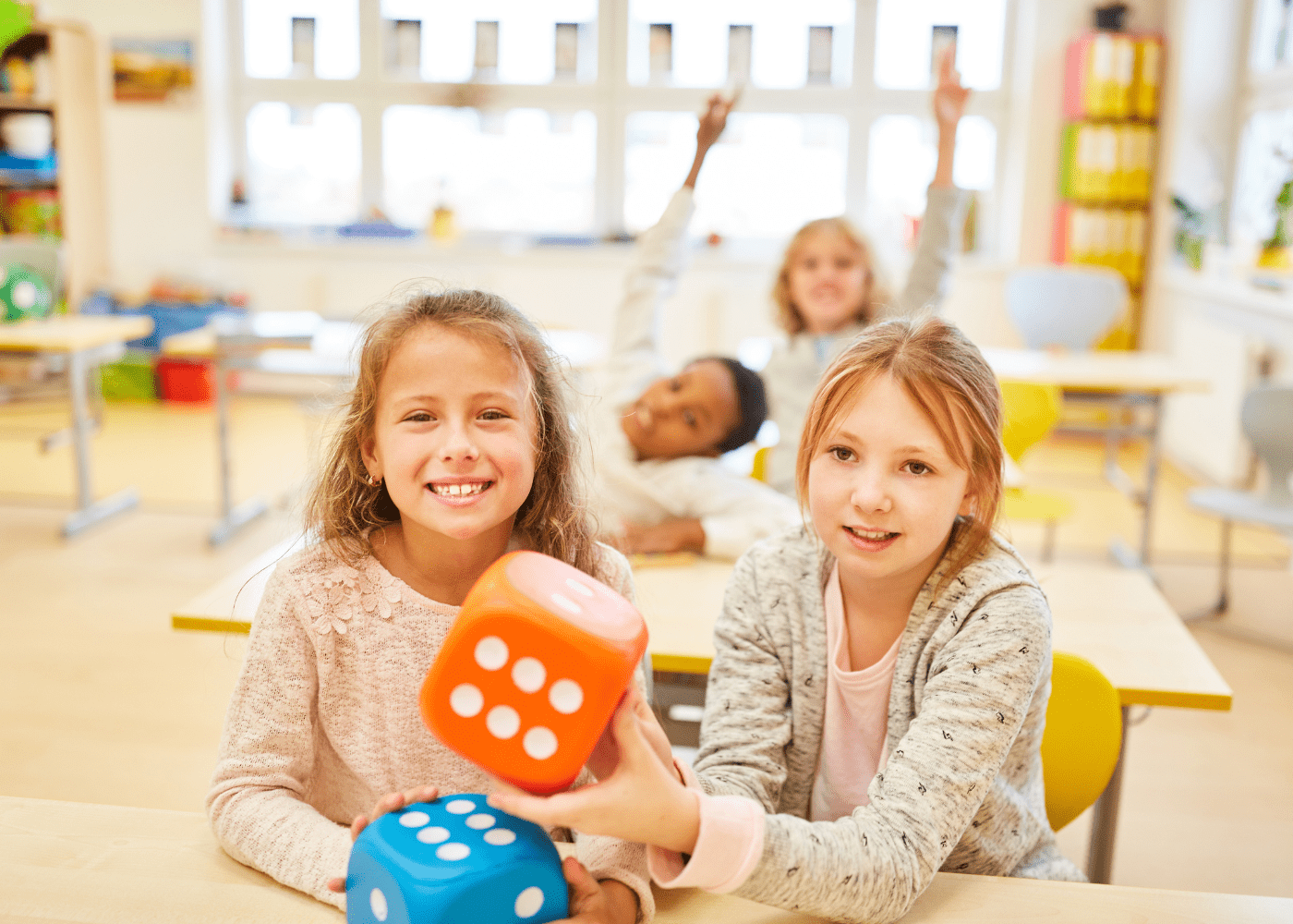 Four children in a classroom with the two in the foreground holding giant dice for a math game.