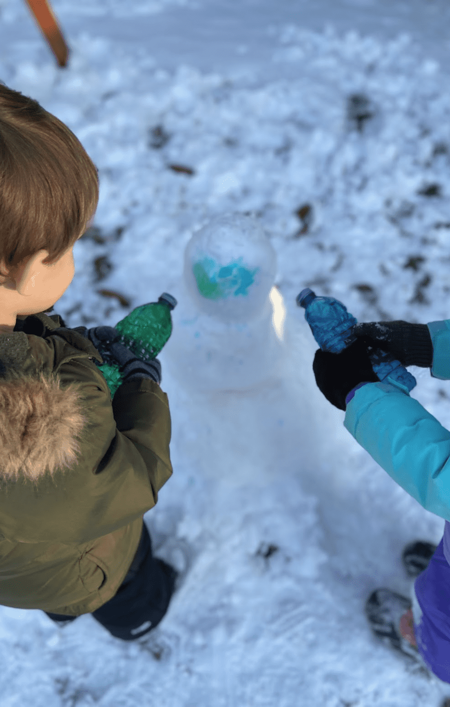 Two children spraying colored water on a snowman.