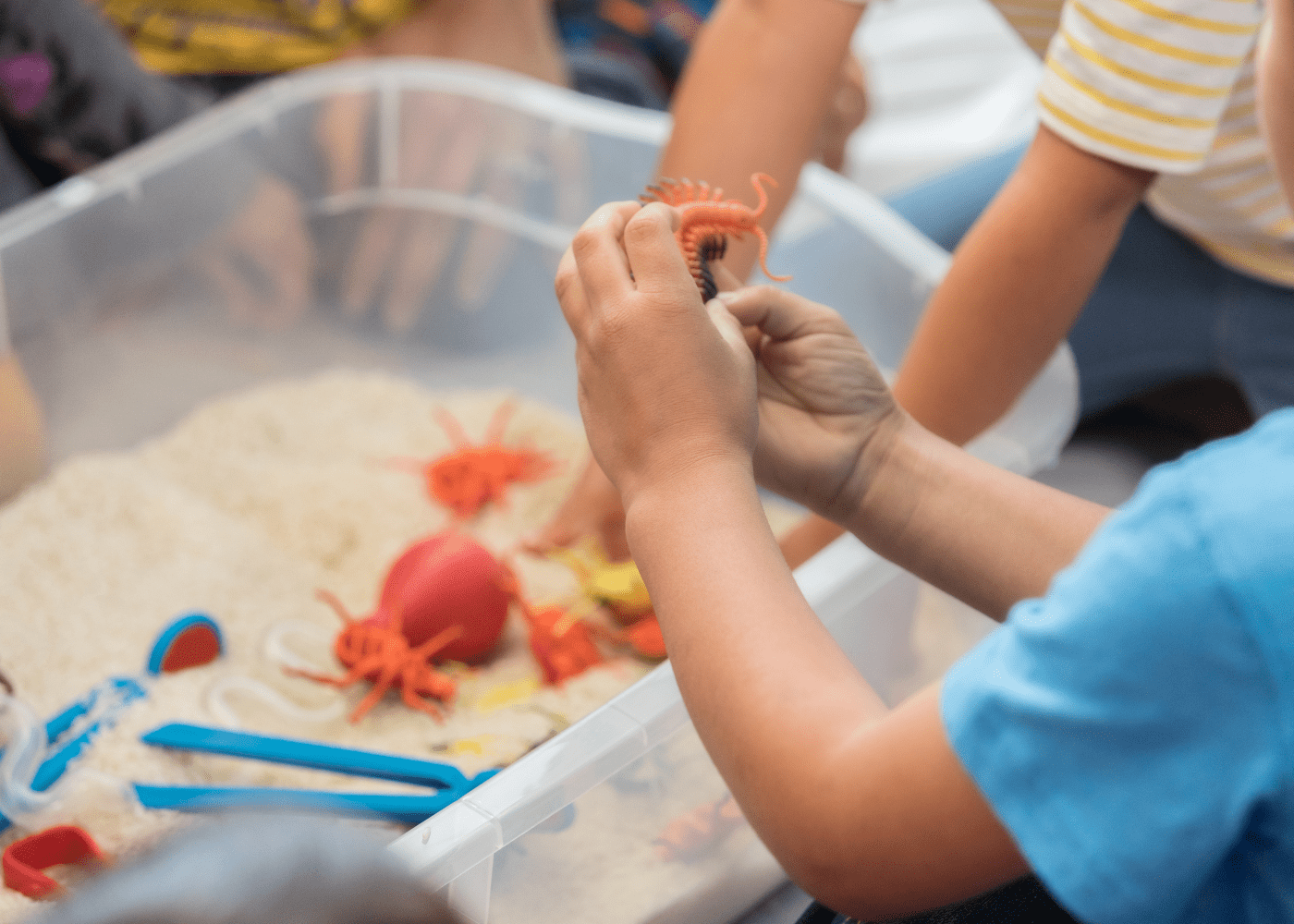 Sensory bin activities for toddlers. They are playing in a bin of rice with fake bugs and tweezers for fine motor development.
