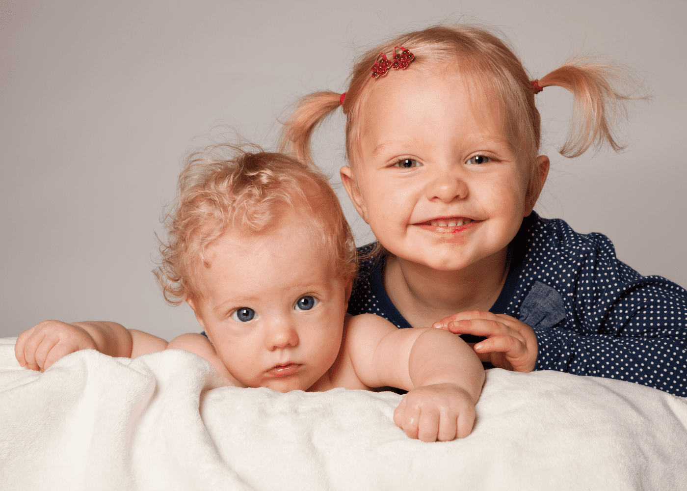 A baby on the left with their big sister on the right smiling.
