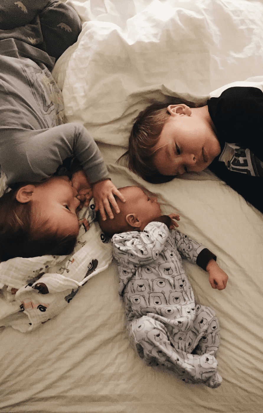 Two older children laying on a bed beside their baby brother.
