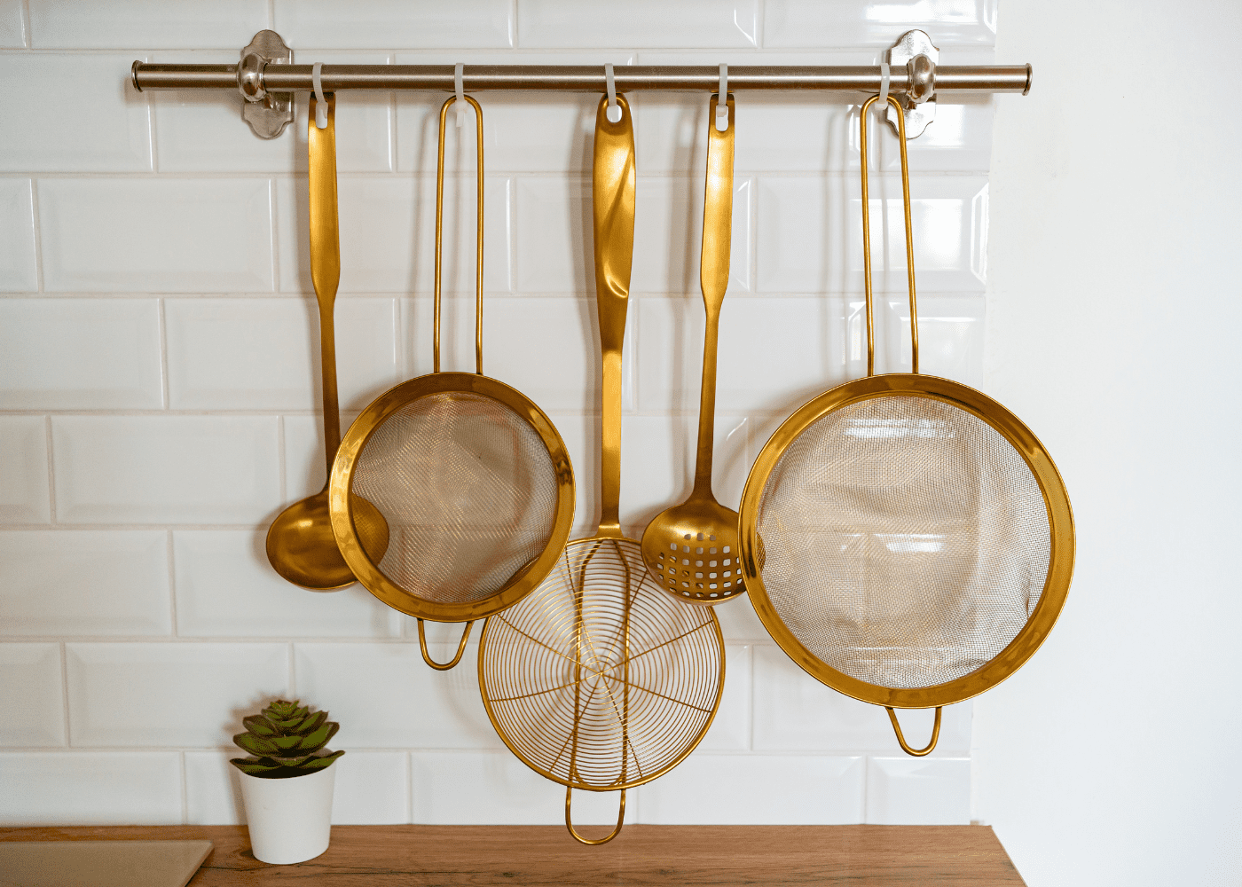 Gold colored kitchen spoons and strainers in front of a white wall