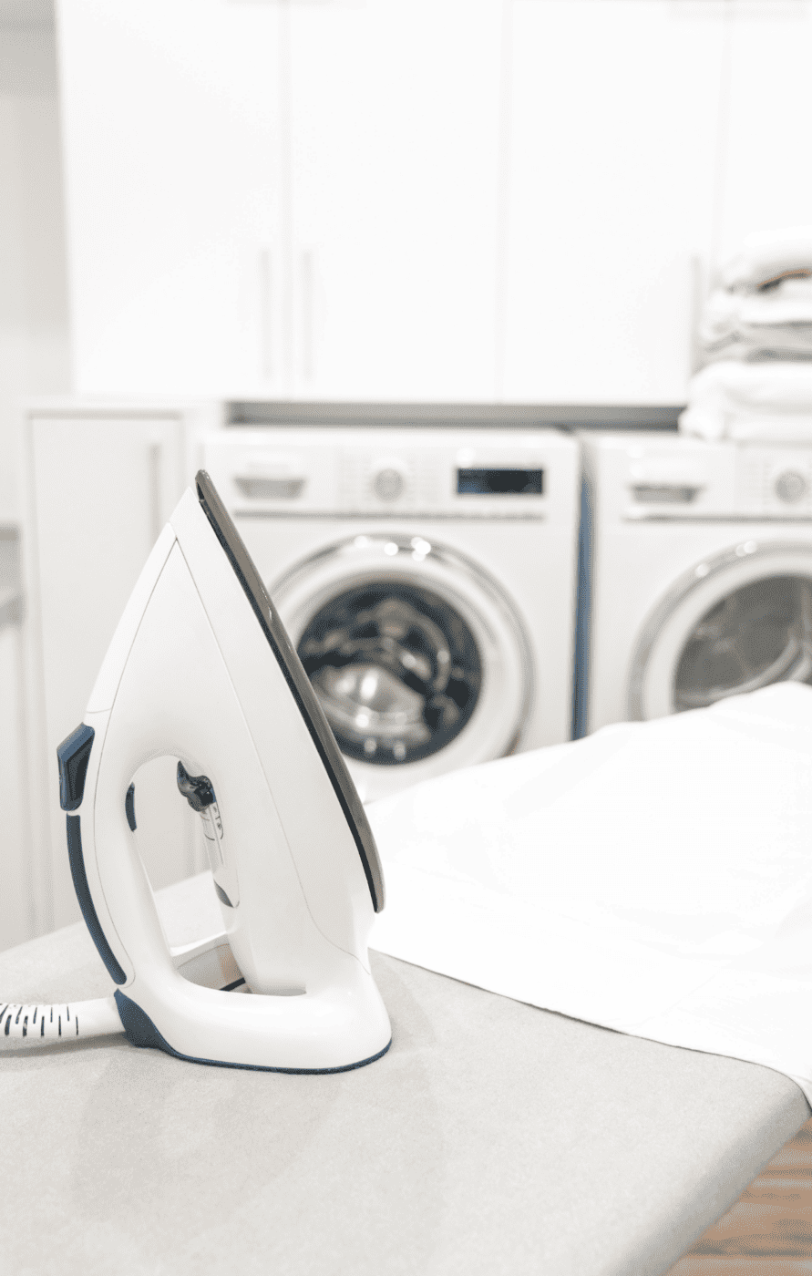 A close up photo of an ironing board and iron in a white laundry room.